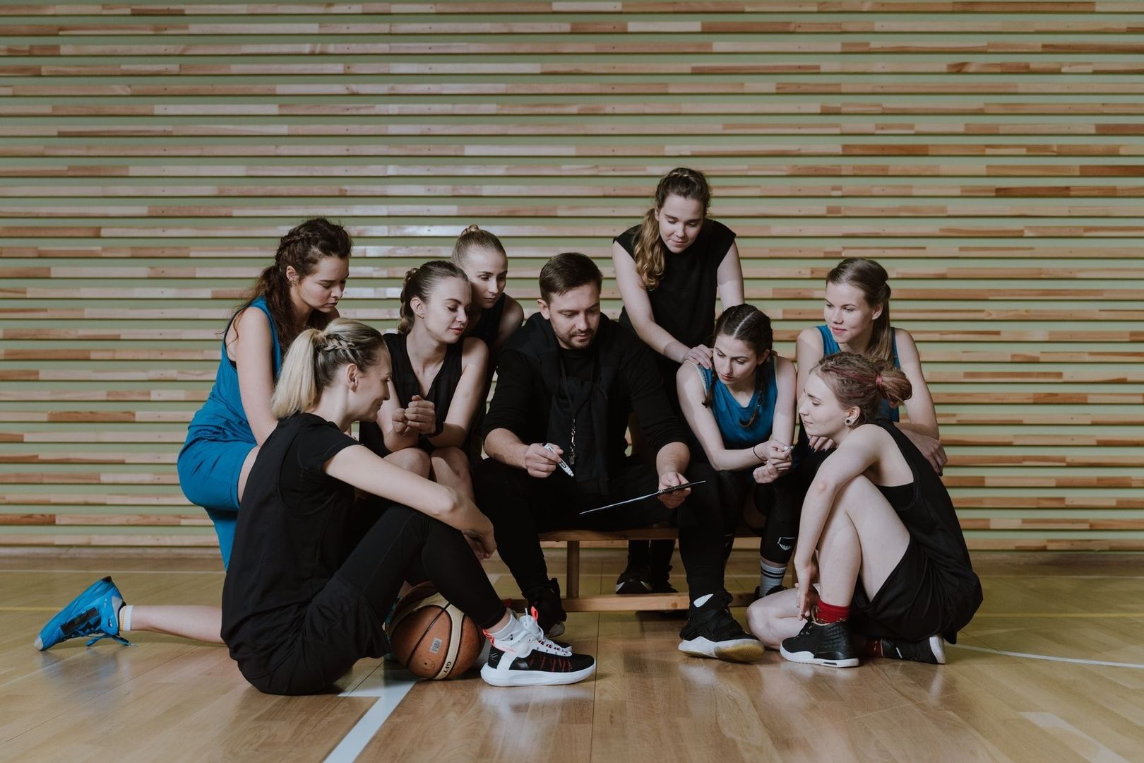 Basketlag samlas kring en tränare med taktiktavla i en idrottshall